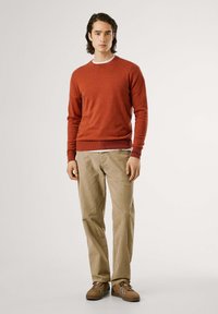 Suéter de punto rojo con cuello redondo, pantalones beiges y zapatos marrones con acentos en azul y blanco. Diseño simple, textura suave.