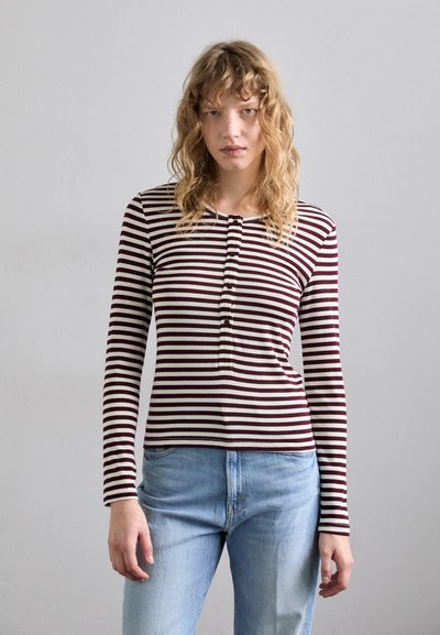 Langärmliges gestreiftes Oberteil in Burgunderrot und Creme mit einer geknöpften Knopfleiste, kombiniert mit hellblauen Jeans. Glattes Material, figurbetontes Design.