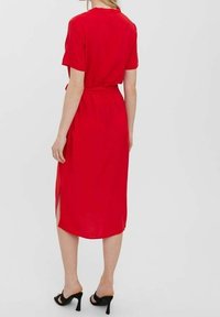 Punainen lyhythihainen mekko, jossa on kapea vyötärö, puolen pituuden muotoilu, sivurei'itykset ja sileä pinta. Yhdistetty mustiin korkokenkiin.