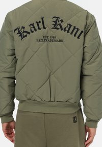 Giubbotto bomber trapuntato verde oliva con loghi ricamati neri sul retro. Polsini e orlo a costine, tessuto leggero e motivo a rombi.