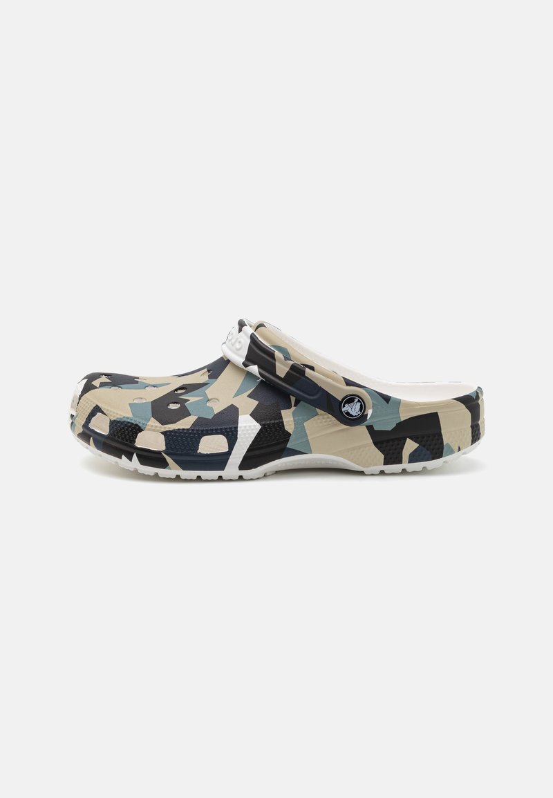 Le sabot présente un motif camouflage en beige, marine et sarcelle, avec une semelle extérieure blanche unie. Fabriqué en matériau flexible et comprend des trous de ventilation.