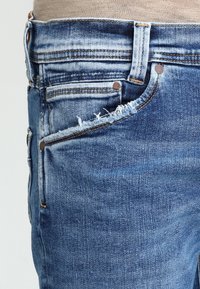 Blå denimjeans med en urtvättad finish, flera fickor och fransade nederkanter. Tyget har en klassisk twillvävstextur.