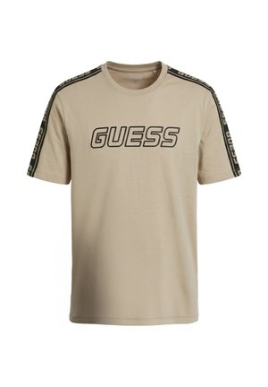 Camiseta beige de manga corta con el logo de GUESS en negro en el frente y franjas negras con la marca a lo largo de los hombros y las mangas.