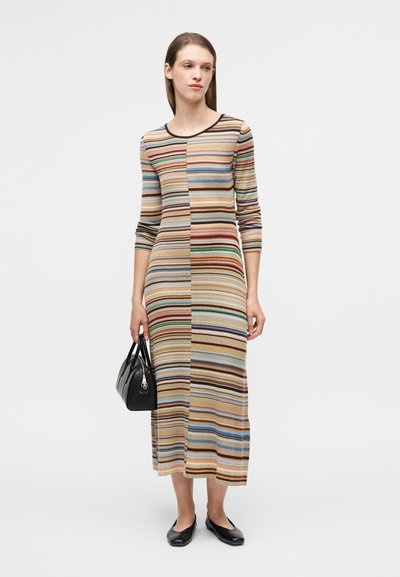Πλεκτό ριγέ φόρεμα με μακριά μανίκια, με εναλλασσόμενα χρώματα καφέ, μπλε και πράσινου, συνδυασμένο με μαύρη τσάντα χειρός και φλατ παπούτσια.