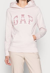 Sudadera con capucha en color rosa claro que presenta un logo gráfico "GAP" con un diseño estampado, con un bolsillo tipo canguro en la parte delantera y puños acanalados.