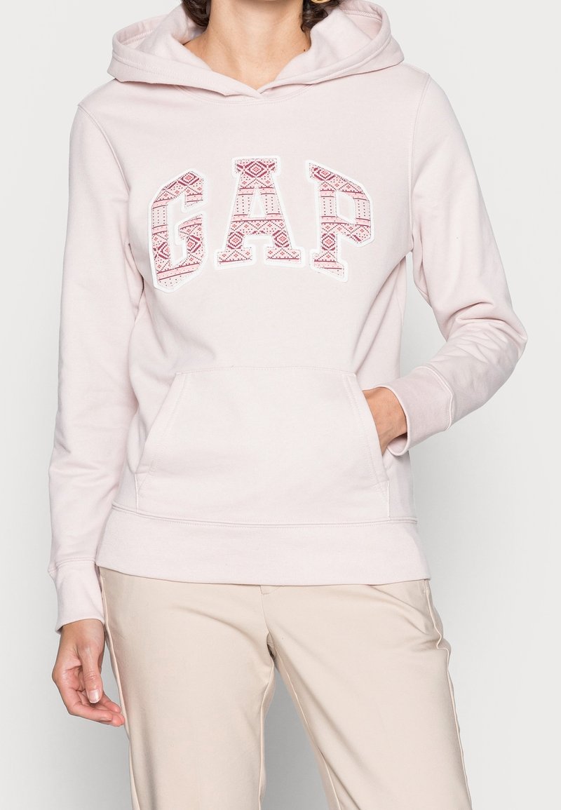 Sudadera con capucha en color rosa claro que presenta un logo gráfico "GAP" con un diseño estampado, con un bolsillo tipo canguro en la parte delantera y puños acanalados.