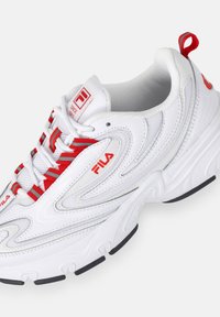 Sneaker sportivo bianco con accenti rossi, materiali in rete e sintetici, superficie texturizzata, logo Fila e suola in gomma con dettagli neri.