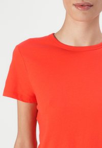 Tricou roșu din bumbac, cu guler rotund și mâneci scurte, având o textură netedă și o formă ajustată. Fără modele sau accente vizibile.