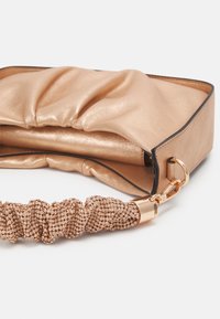 Metallic beige clutch med en samlet satin-design, der har et glitrende perle-håndtag og en glat, flad bund. Accentueret med guldhardware.