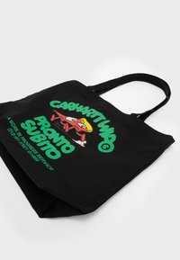 Black canvas tote bag with green and red graphic text and cartoon character. Features two shoulder straps and a large open compartment.