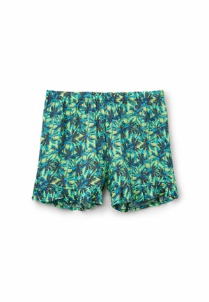 Shorts verts courts avec un motif de feuilles de palmier bleues et foncées, et une taille élastique sur fond blanc.