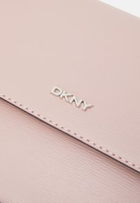 Portafoglio DKNY rosa chiaro con superficie texturizzata, logo argentato e dettaglio di cucitura a contrasto lungo i bordi. Design compatto ed elegante.