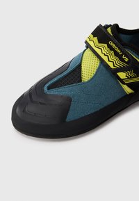 Shoe za penjanje s tamnoplavim nubuk gornjim dijelom, crnim gumenim potplatom, mrežastim akcentima i žutim remenom s dizajnom u obliku cik-caka za sigurno prianjanje.