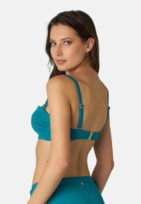 Reggiseno verde acqua con spalline regolabili, caratterizzato da dettagli arricciati e accessori in tono dorato. Texture liscia e design semplice.