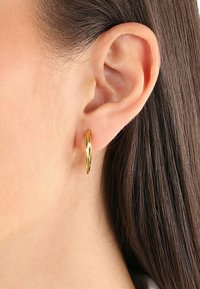 Pendientes de aro de oro con un diseño trenzado, de grosor medio y textura suave, que complementan la oreja sin sujetadores visibles.