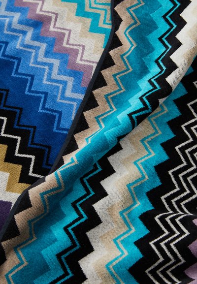 Tessuto intrecciato con un motivo a zigzag in tonalità di blu, nero, beige e viola. Texture morbida con un design geometrico prominente.