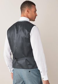 Graues Satin-Westen mit tailliertem Rückenteil, verstellbarem Trageriemen und glatter Oberfläche. Kombiniert mit einem weißen Hemd mit geknöpften Manschetten und blauen Akzenten.