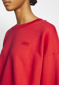 Czerwona bluza wykonana z miękkiej bawełny, z okrągłym dekoltem, luźnym krojem i haftowanym logo "LEVI'S" na piersi. Gładka tekstura.