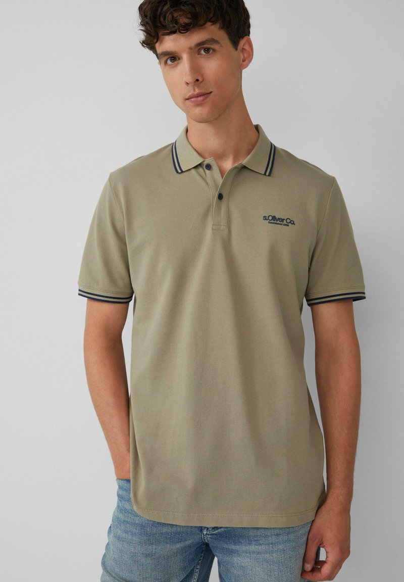 Jasnozielona koszulka polo z granatowymi paskami na kołnierzyku i rękawach, z dwoma guzikami przy plastrze i haftowanym logo na piersi.