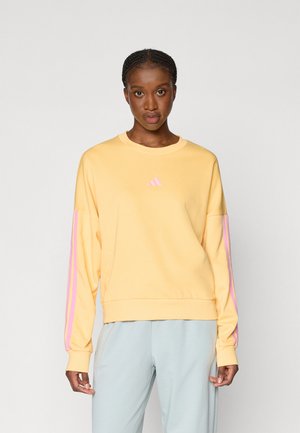 Gul genser med rosa striper på ermene, rund halslinning og en liten rosa logo på brystet. Mykt stoff og avslappet passform.