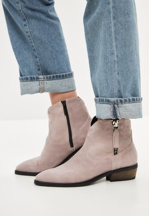 Lichtgrijze suède enkellaarzen met een spitze neus, een rits aan de zijkant en een lage blokhak, gedragen met opgerolde blauwe jeans.