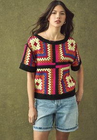 Kuka majica s živopisnim bojama, geometrijskim uzorcima u nijansama ružičaste, narančaste, plave i žute, s crnim rebrastim rubom i kratkim rukavima.