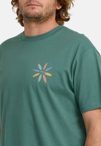 Grøn T-shirt lavet af bomuld, med et farverigt surfbræt grafik på venstre brystområde. Rund hals design og korte ærmer.