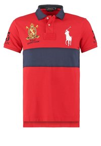 Polo rouge avec une rayure horizontale bleu marine. Comprend un logo brodé et le numéro 3 sur les manches. Col classique et manches courtes. Tissu en coton.