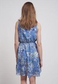 Kleid mit floralem Muster in Hellblau, ärmellos, mit elastischem Bund und schwingendem Rock. Es zeigt verschiedene kleine Blumen und Grünpflanzen.