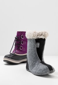 Set di calzature: stivale impermeabile viola scuro con lacci e suola in gomma nera, e stivale in feltro grigio con risvolto in pelliccia bianca e dettagli neri.