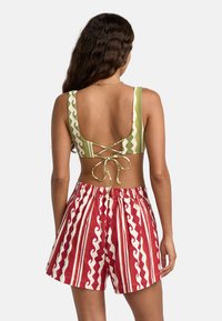 Haut de bikini à motifs verts avec un dos décolleté et un design entrecroisé ; assorti à un short rayé rouge et blanc avec des motifs de vagues.