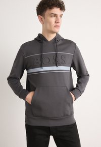 Felpa con cappuccio grigio scuro, con tasca a marsupio frontale, caratterizzata da un logo "BOSS" in rilievo e una striscia orizzontale azzurro chiaro.
