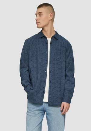 Marineblauw overhemd met knopen, voorzien van een gestructureerd geometrisch patroon, lange mouwen, klassieke kraag en een enkele borstzak, gecombineerd met lichte jeans.
