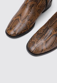 Bottes en cuir à imprimé serpent marron avec un bout pointu et une surface texturée, présentant une semelle noire élégante et une finition sans coutures.