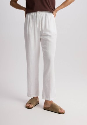 Białe lniane spodnie o luźnym kroju, z elastycznym pasem i sznurkiem do regulacji. Połączone z beżowymi klapkami.