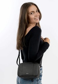 Černá crossbody taška z texturované kůže, obdélníkového tvaru, se stříbrným logem. Disponuje odnímatelným popruhem a minimalistickým designem.