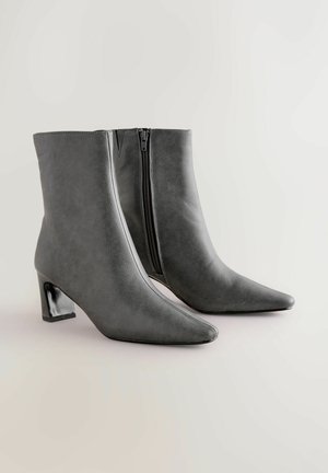 Gray faux leather ankle boots with a pointed toe, block heel, and side zipper. Smooth texture, minimalist design, and sleek silhouette.