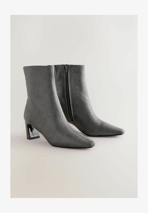 Šedé kožené kotníkové boty s špičatou špičkou, blokovým podpatkem a bočním zipem. Hladký povrch, minimalistický design a elegantní silueta.