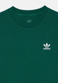 Zelené bavlněné tričko s kulatým výstřihem. Na levé části hrudníku je vyšívané bílé logo Adidas. Měkká textura.
