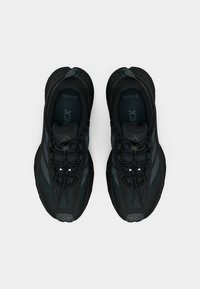 Černé sportovní boty s текстilní síťovinou, strukturovaným svrškem a vzorovanými detaily. Mají tkaničky, zesílenou patu a polstrovanou podrážku.