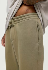 Khaki joggerbroek gemaakt van zachte katoenmixstof met een trekkoord van de taille, zijzakken en geribbelde details op de tailleband.