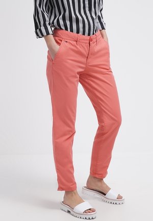 Korallenfarbene Slim-Fit-Hosen aus Baumwolle mit Seitentaschen, Gürtelschlaufen und einer glatten Textur. Kombiniert mit weißen Sandalen.