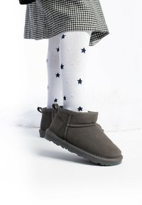 Botas de tobillo de ante gris con puntera redondeada y tira de agarre, combinadas con calcetas blancas con patrones de estrellas en azul marino. Falda de pata de gallo visible arriba.