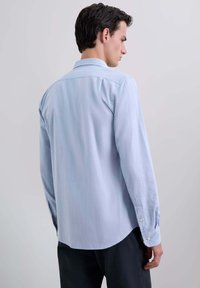 Camisa de manga larga azul claro hecha de una tela suave, con cuello abotonado, dobladillo redondeado y puños de un solo botón.