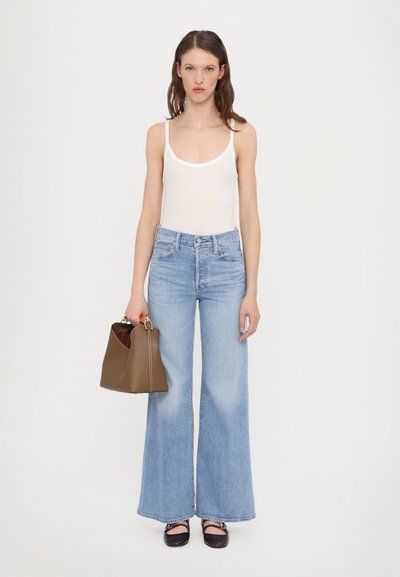 Wide-leg light blue jeans, white tank top, brown handbag with gold hardware, and black shoes. Focus on tailored fit and casual style.