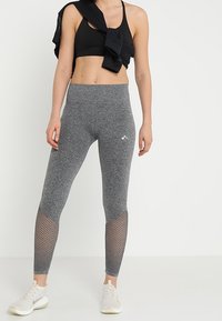 Szare legginsy sportowe o dopasowanym kroju, z siateczkowym akcentem na dolnej części nogawki. W zestawie z czarnym stanikiem sportowym i jasnymi sneakersami.