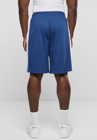 Marine atletikshorts lavet af letvægtsmateriale, med hvide sidelæder, en elastisk talje og en løs pasform. Stylings med hvide sneakers.