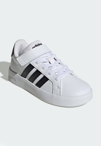 Bijela atletska cipela s crnim dizajnom tri pruge. Izrađena od sintetičke kože, s jastučićem oko gležnja, vezicama sprijeda i gumenom potplatom.