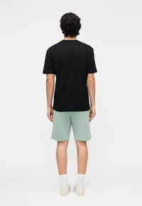 Zwart katoenen T-shirt gecombineerd met lichtgroene korte broek. De outfit heeft een losse pasvorm en een zachte textuur, geschikt voor casual gebruik.