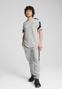 Harmaa urheilupaita ja housut mustilla ja turkooseilla yksityiskohdilla; molemmissa, niin paidassa kuin housuissa, on logot; teksturoitu kangas; rento istuvuus.